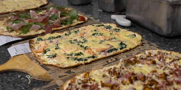 Mehrere verschiedene, frisch gebackene Flammkuchen auf rustikalen Servierbrettern.