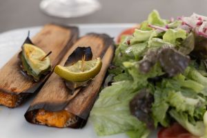 Zwei kleine Holzröllchen mit gegrilltem Fisch, garniert mit Lorbeerblatt und Zitronenscheibe, daneben ein frischer grüner Salat.