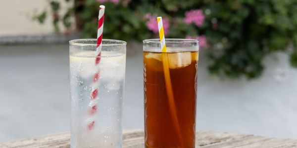 Zwei hohe Gläser in denen jeweils ein Papierstrohalm steckt, gefüllt mit Limonaden und Eis.