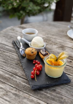 Ein Dessert-Arrangement auf einer schwarzen Schieferplatte mit Espresso, Vanilleeis, Mini-Muffin, Éclair, Crème brûlée und Johannisbeeren.