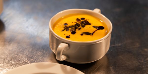 Eine weiße Suppentasse mit cremiger Kürbissuppe, verfeinert mit gerösteten Kürbiskernen und dunklem Kürbiskernöl.