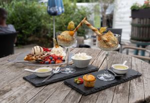 Ein üppiges Dessert-Ensemble, bestehend aus zwei Eisbechern mit Engelshaar und Waffelröllchen, einer belgischen Waffel mit Beeren und Eis sowie kleinen Saucen.