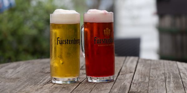 Zwei Gläser Bier mit Schaumkrone, ein helles und ein rötliches, stehen nebeneinander auf einem Holztisch.