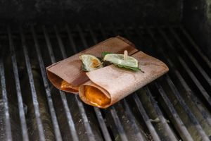 Zwei kleine Holzröllchen mit Fisch, garniert mit Limettenscheibe und Lorbeerblatt, garen direkt auf einem Grillrost.