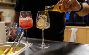Ein Barkeeper gießt Getränke aus kleinen Crodino-Flaschen in zwei mit Eis gefüllte Gläser ein.