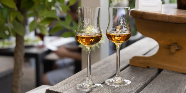 Zwei gefüllte Gläser Grappa stehen auf einem Holztisch, daneben ein kleiner Aufsteller eines Restaurants.