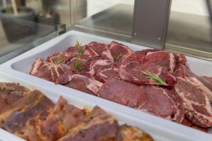 Eine Auslage mit rohen Rindersteaks und mariniertem Fleisch in weißen Schalen, garniert mit frischen Rosmarinzweigen.