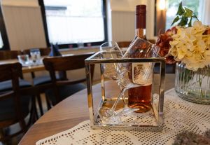 Eine Flasche Roséwein und zwei leere Weingläser stehen in einem dekorativen, quadratischen Metallhalter auf einem Tisch mit weißer Tischdecke.