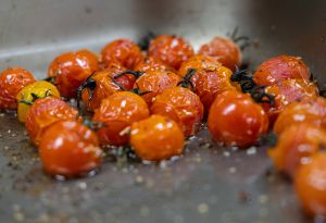 Eine Nahaufnahme von vielen kleinen, gerösteten Kirschtomaten in einer Metallschale.