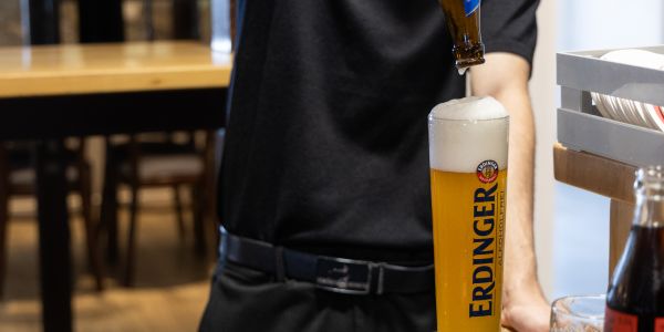 Ein Barkeeper schenkt alkoholfreies Weißbier fachgerecht aus der Flasche in ein passendes Weißbierglas ein.