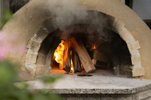 Ein traditioneller, gemauerter Holzofen, in dessen Innerem ein loderndes Holzfeuer brennt.