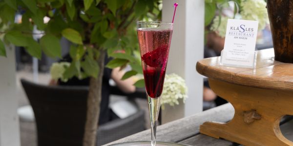 Ein hohes, schmales Glas mit einem leuchtend roten Aperitif und einer roten Einlage, daneben ein Aufsteller mit Visitenkarten.